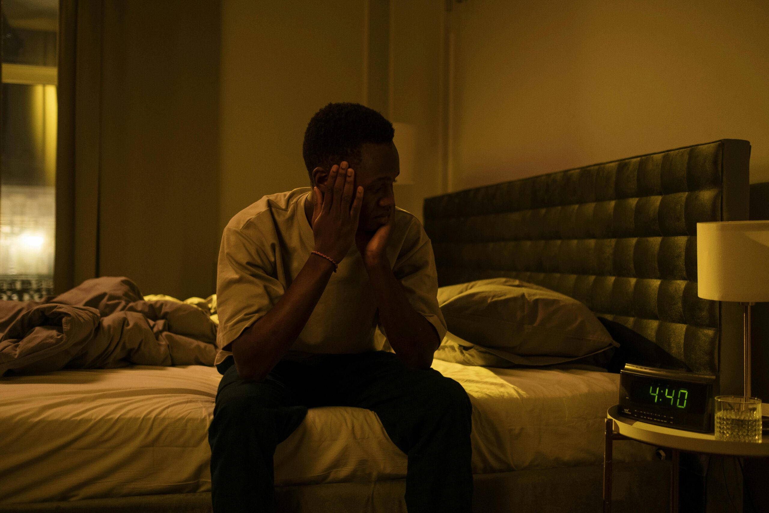 African American man sitting on a bed struggling with insomnia at night.